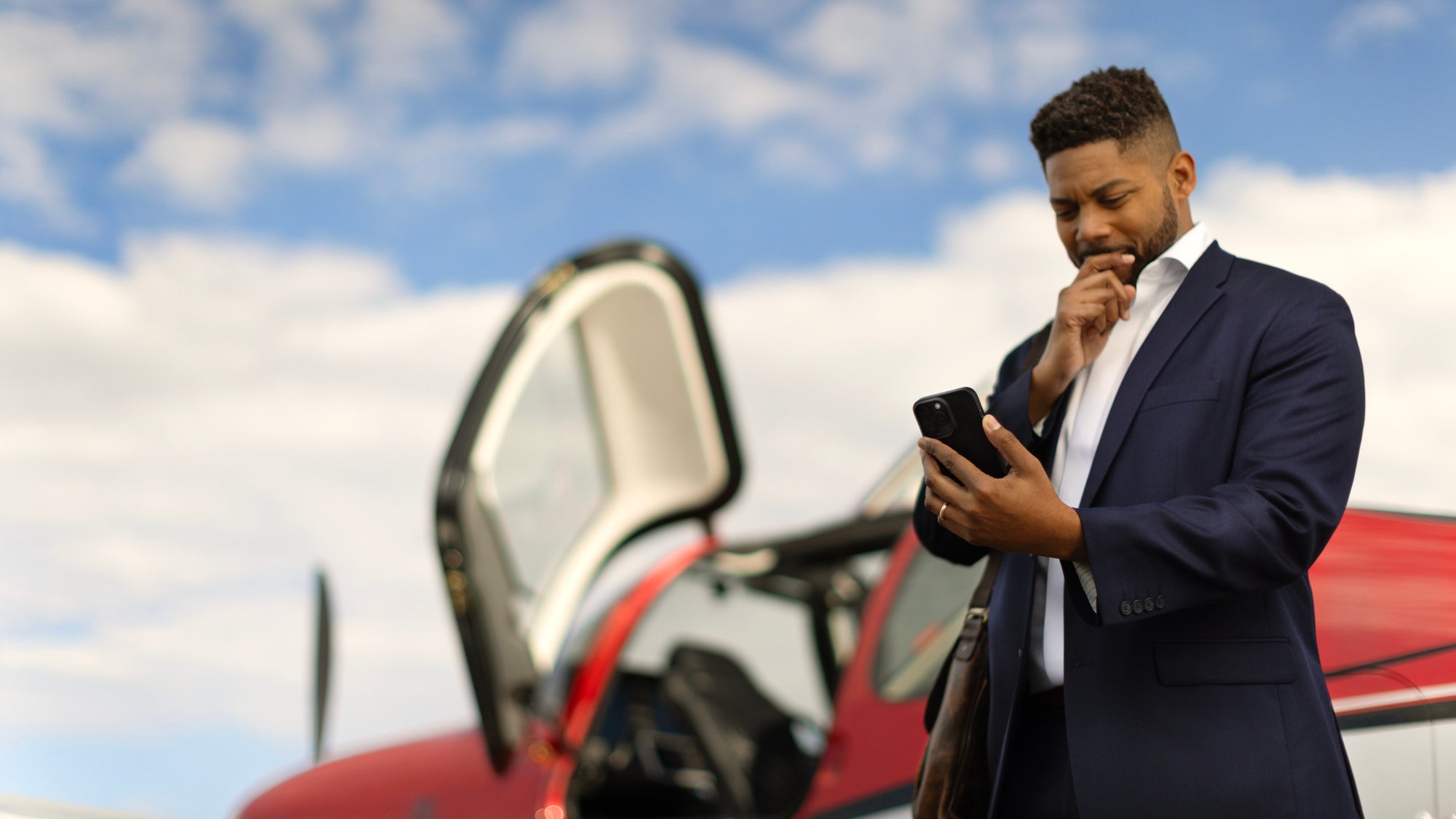 business man looking at phone in front of red cirrus plane