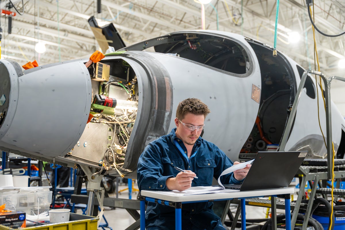 cirrus employee sitting at his desk looking over plans with plane shell behind him