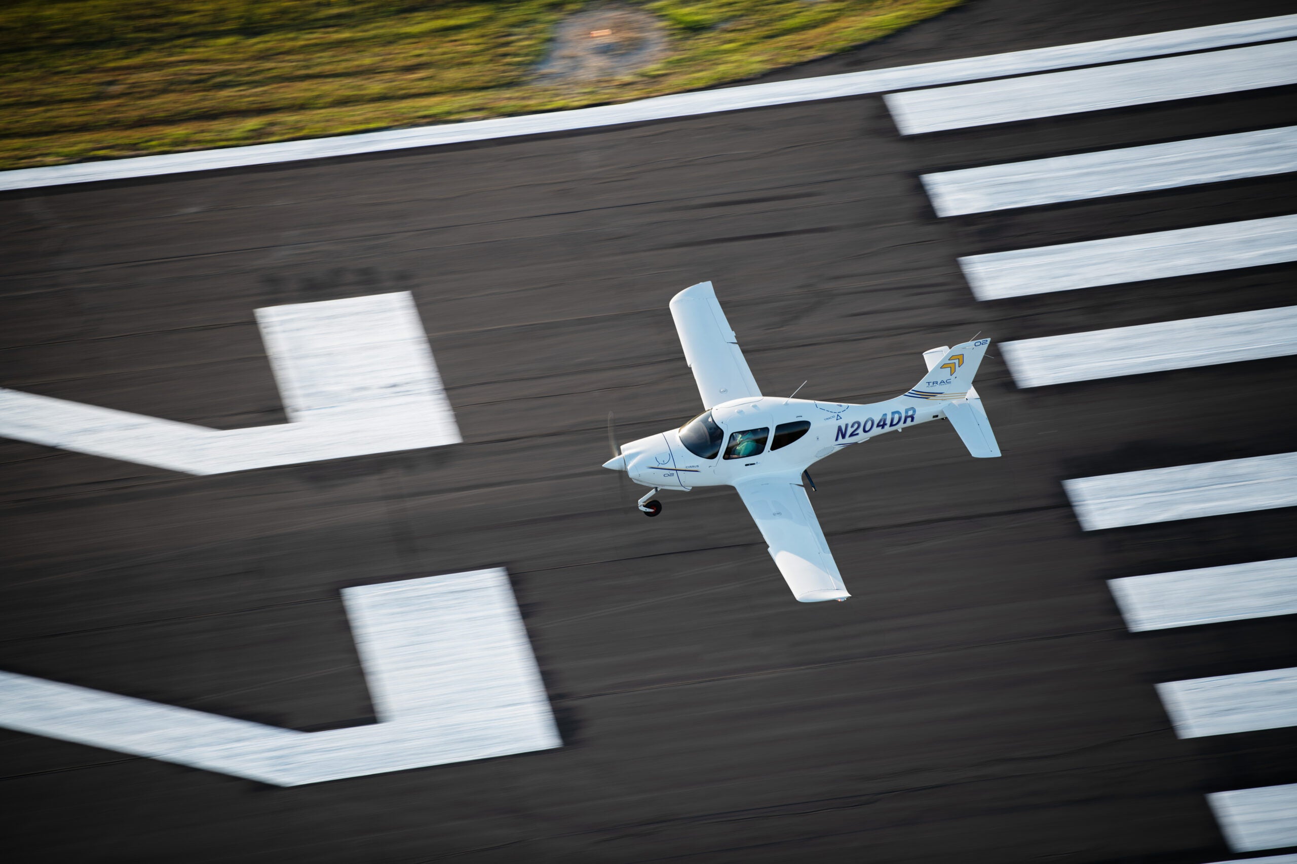 Overhead view of a Cirrus TRAC10 training aircraft flying low over a runway