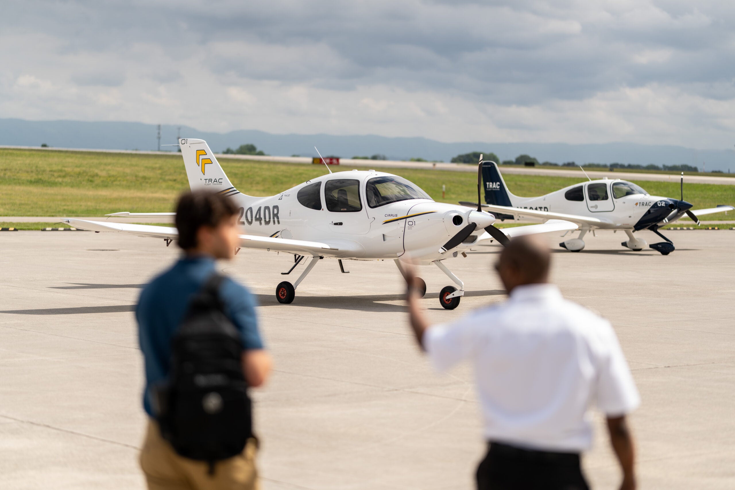 Two Cirrus TRAC10 flight training aircraft parked on the ramp as a student and instructor look on