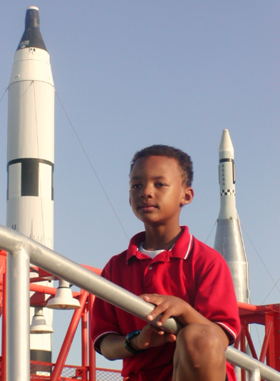A young Josh Dobbs standing in front of space rockets on display at the Kennedy Space Center