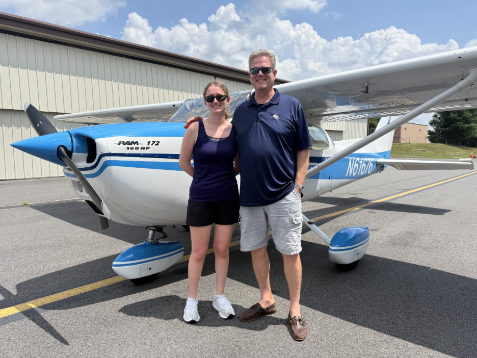 Maddie Allen and her father standing in front of a blue and white single-engine trainer outside a hangar