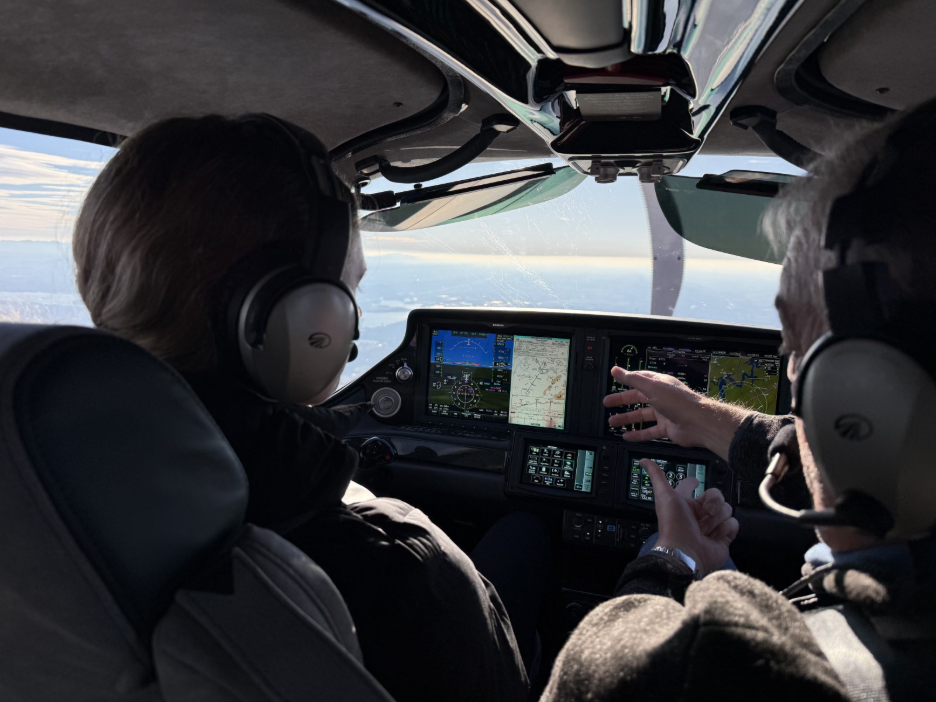 View from behind two pilots in a Cirrus SR Series flight deck with the avionics displays lit in cruise flight