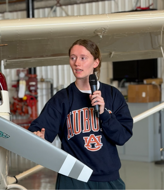 Maddie Allen speaking into a microphone beside an aircraft propeller in a hangar at Auburn University