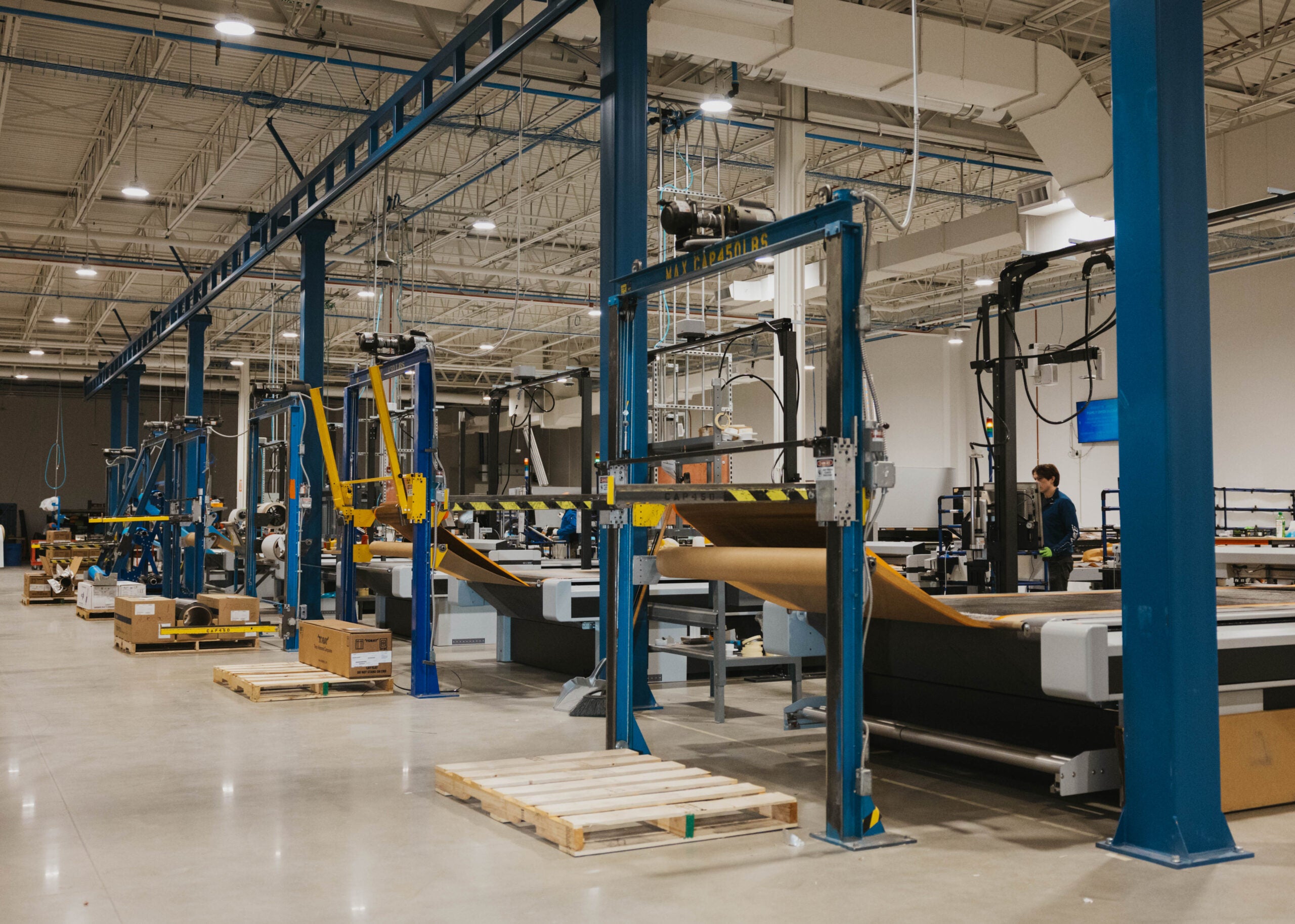 Interior of the expanded Cirrus Grand Forks facility showing overhead gantries and composite cutting tables