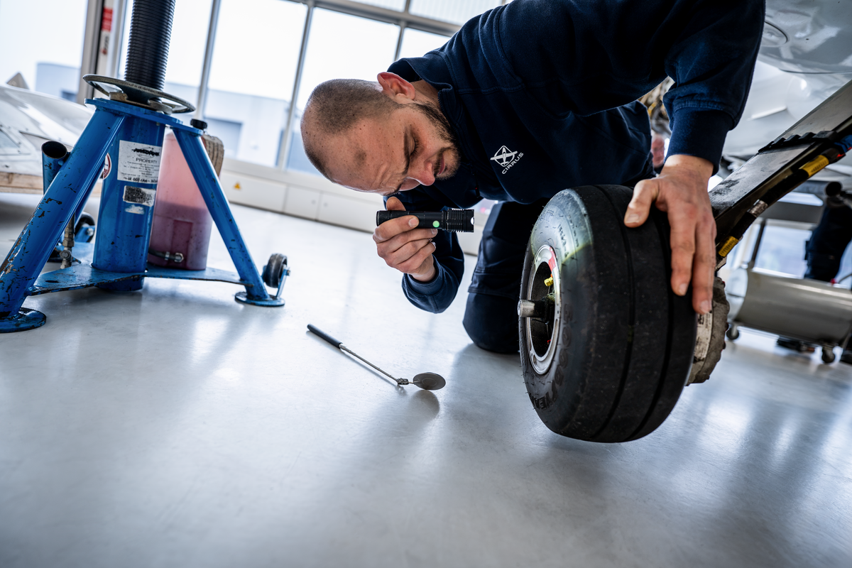 Technician inspecting the main landing gear tire of a Cirrus aircraft with a flashlight