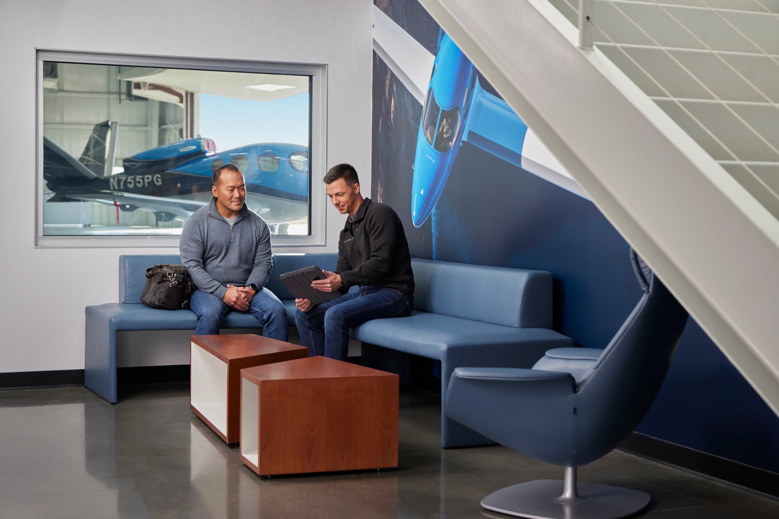 Two customers talking on a couch in a Cirrus service center lounge with aircraft outside