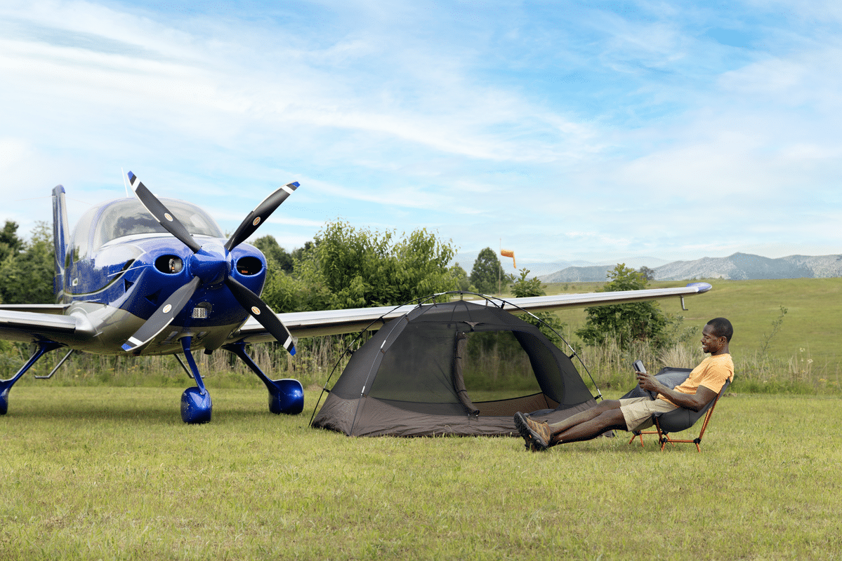 man reading while camping next a blue cirrus airplane